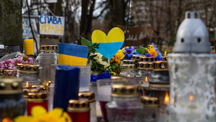 Candles, flowers and small Ukrainian flags on the pedestrian sidewalk in memory of those killed in...