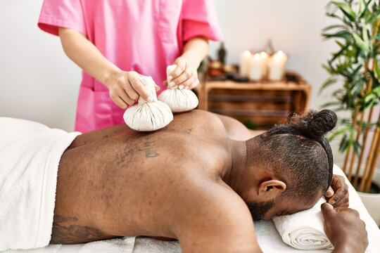 Young african american man having back massage with thai bags at beauty center