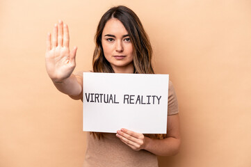 Fototapeta na wymiar Young caucasian woman holding a virtual reality placard isolated on beige background standing with outstretched hand showing stop sign, preventing you.