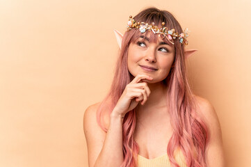 Naklejka premium Young elf woman with pink hair isolated on beige background looking sideways with doubtful and skeptical expression.