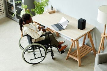 High angle view of young African American woman in wheelchair using laptop while working at home...