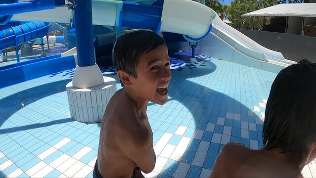 Young happy, confident and cocky multiracial twin boys make faces then run away at a waterpark. Slow motion.