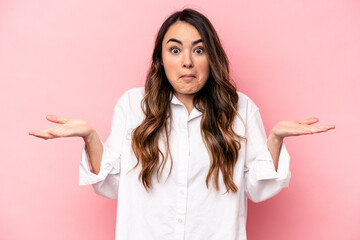 Young caucasian woman isolated on pink background doubting and shrugging shoulders in questioning...