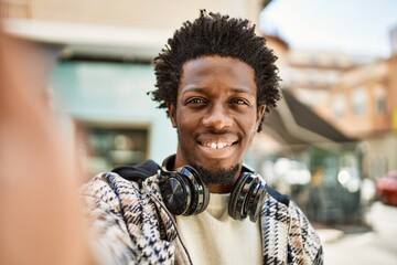 Handsome black man with afro hair wearing headphones smiling happy outdoors taking selfie picture