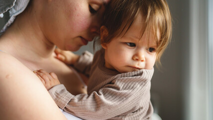 Caucasian woman mother holding his small baby girl while standing by the window at home looking to the side real people parenthood bonding love and family concept copy space