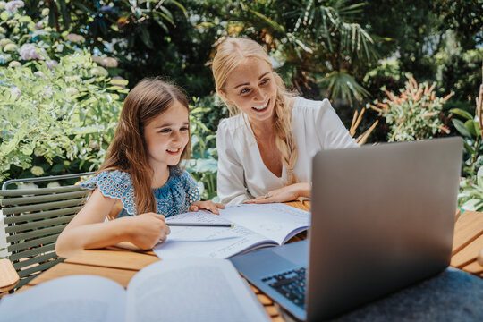 Smiling mother and daughter in online education over laptop at back yard