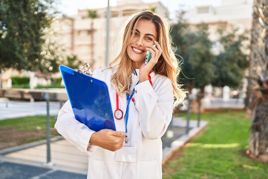 Young blonde woman wearing doctor uniform talking on the smartphone at park