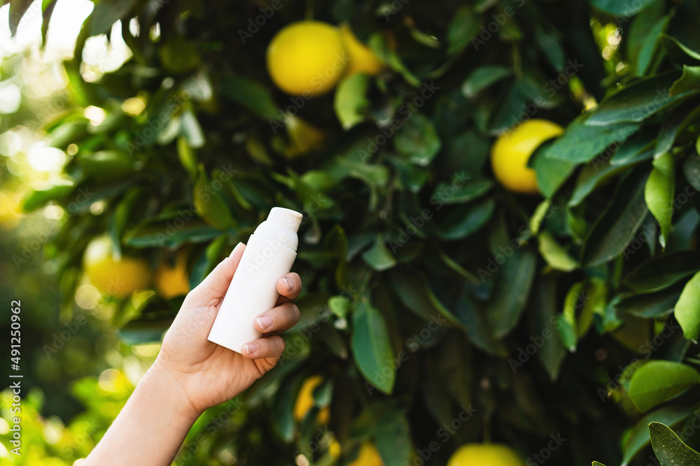 Wall mural Woman holds bottle of skin care product in her hand on lemon tree background.