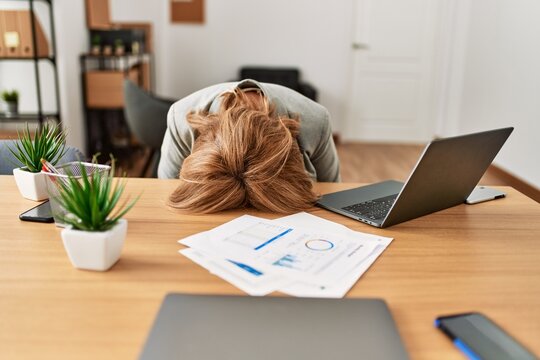 Middle age businesswoman overworked with head on desk at the office.