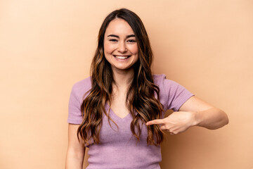 Young caucasian woman isolated on beige background person pointing by hand to a shirt copy space, proud and confident