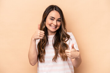 Young caucasian woman isolated on beige background raising both thumbs up, smiling and confident.