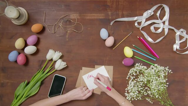 Top view of a table with items to create a composition for Easter. A woman's hand writes with a red marker: Happy Easter. Christ is risen. Church holiday-Easter