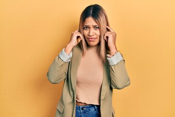 Beautiful hispanic woman wearing business jacket covering ears with fingers with annoyed expression for the noise of loud music. deaf concept.