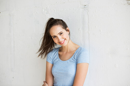 Happy woman with ponytail standing in front of wall