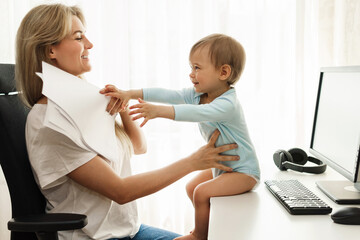 Little boy sitting on a desk distracting freelancer mother from paperwork.