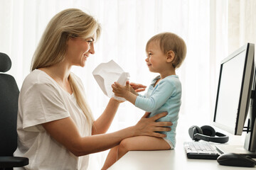 Little boy sitting on a desk distracting freelancer mother from paperwork.
