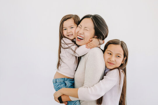 Cute daughters embracing happy mother by white background