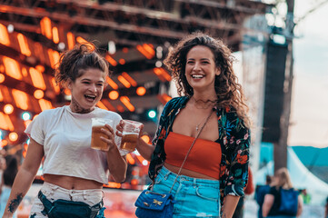 Two beautiful friends drinking beer and having fun on a music festival