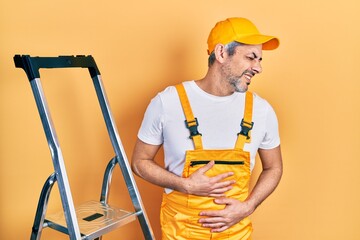 Handsome middle age man with grey hair holding ladder with hand on stomach because nausea, painful disease feeling unwell. ache concept.