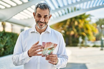 Middle age grey-haired man smiling happy counting new zealand dollars at the city.