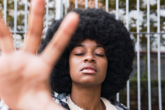 Afro woman with eyes closed showing palm in front of fence
