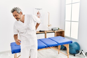 Fototapeta premium Middle age hispanic therapist man working at pain recovery clinic suffering of backache, touching back with hand, muscular pain