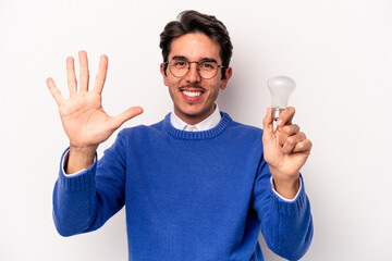 Young caucasian man holding a lightbulb isolated on white background smiling cheerful showing number five with fingers.