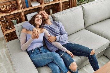 Young caucasian couple relaxed sitting on the sofa hugging at home.