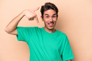 Obraz premium Young caucasian man isolated on beige background person pointing by hand to a shirt copy space, proud and confident