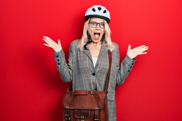 Beautiful caucasian blonde business woman wearing bike helmet celebrating crazy and amazed for...
