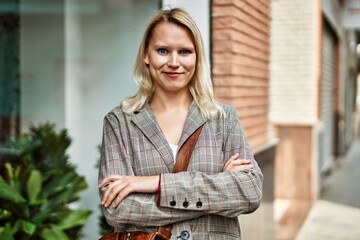 Young blonde businesswoman smiling happy with arms crossed gesture at the city.