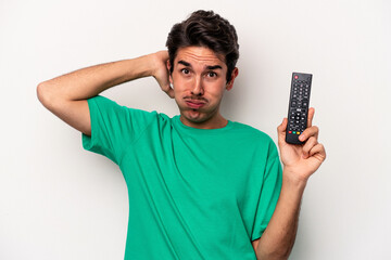 Young caucasian man holding a tv remote isolated on white background being shocked, she has...