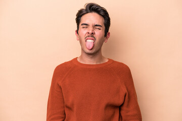 Young caucasian man isolated on beige background funny and friendly sticking out tongue.