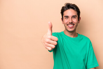 Young caucasian man isolated on beige background smiling and raising thumb up