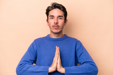 Young caucasian man isolated on beige background praying, showing devotion, religious person looking for divine inspiration.