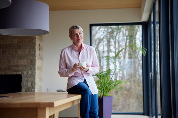 Blond woman holding coffee cup sitting on table at home