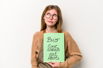 Young gardener woman holding a bio placard isolated on white background dreaming of achieving goals and purposes