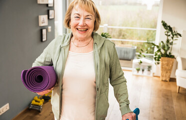 Cheerful senior woman with exercise mat at home