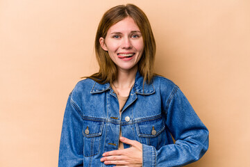 Young English woman isolated on beige background touches tummy, smiles gently, eating and satisfaction concept.