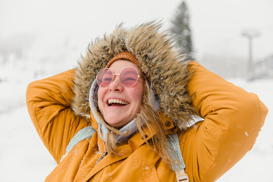 Happy woman in fur jacket enjoying snowfall at vacation
