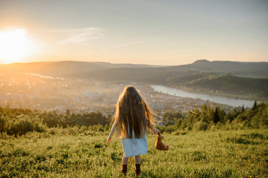 Girl with long hair holding stuffed toy standing on meadow