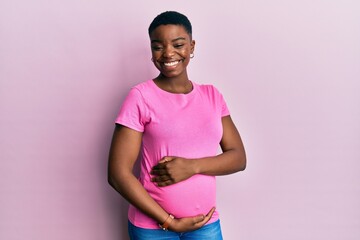 Young african american woman expecting a baby, touching pregnant belly winking looking at the...