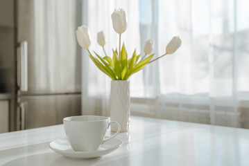White tulips in a vase and a white cup on the table