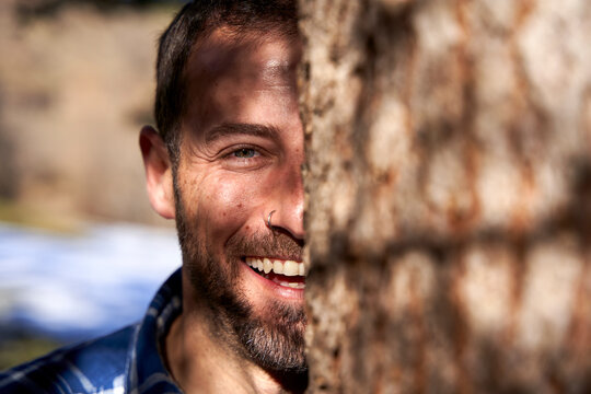 Happy man behind tree truck on sunny day