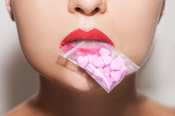 Woman holding ziplock bag with pink pills in her mouth.