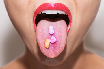 Female face with colorful vitamin or drug pills on her tongue