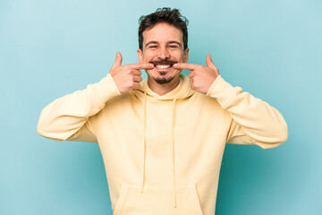 Fototapeta premium Young caucasian man isolated on blue background smiles, pointing fingers at mouth.