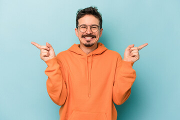 Fototapeta premium Young caucasian man isolated on blue background pointing to different copy spaces, choosing one of them, showing with finger.