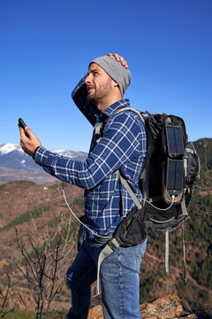 Man wearing backpack holding smart phone charged through portable solar panel on sunny day
