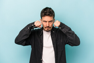 Fototapeta premium Young caucasian man isolated on blue background throwing a punch, anger, fighting due to an argument, boxing.